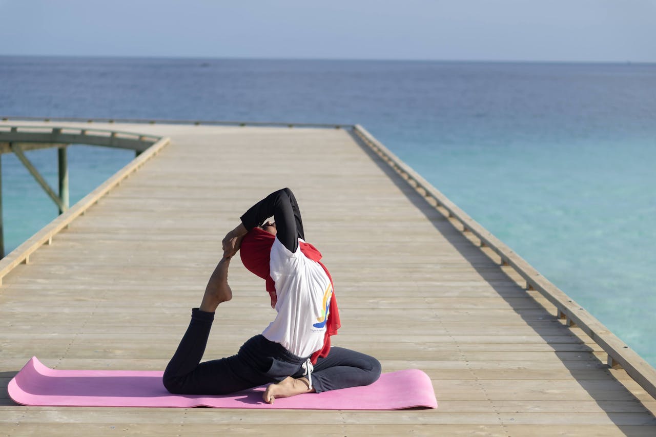 A person in a yoga pose on a wooden pier, with tranquil ocean and clear sky.