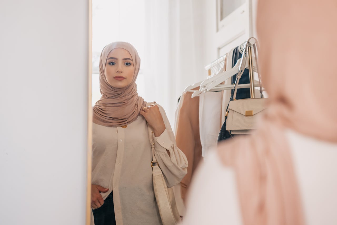 Young woman in hijab admiring herself in the mirror, showcasing elegance and style indoors.